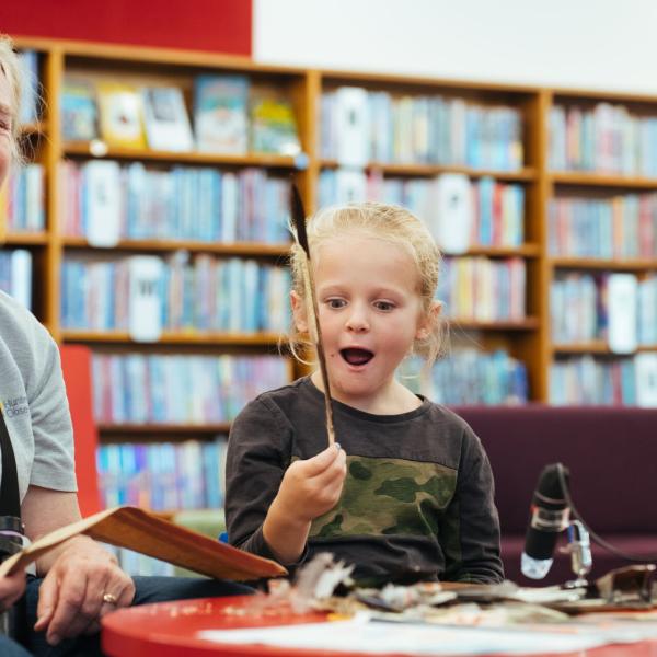 Child holding up a feather at a library