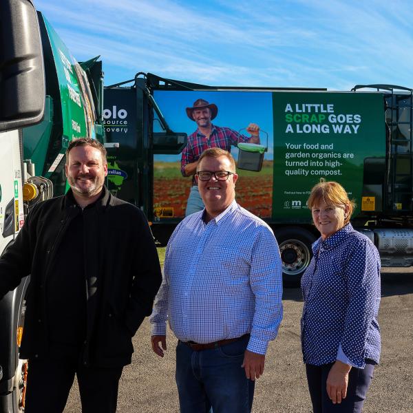 Three people stand in line smiling with large waste trucks in background with FOGO branding.
