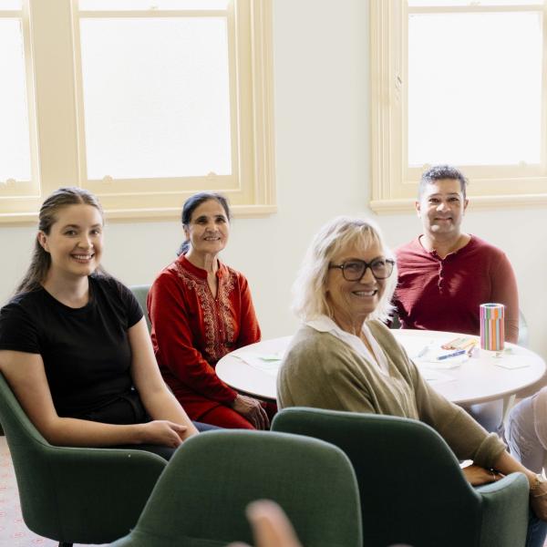 A group of four people sit around a table, looking at a person who is offscreen.