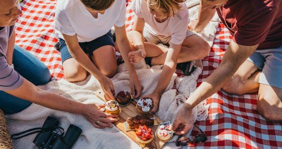 Family reaching for pastries on a picnic rug