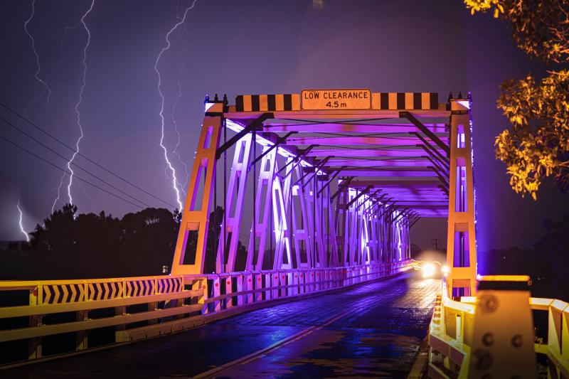 Morpeth Bridge lit up with purple lights & lighting striking behind