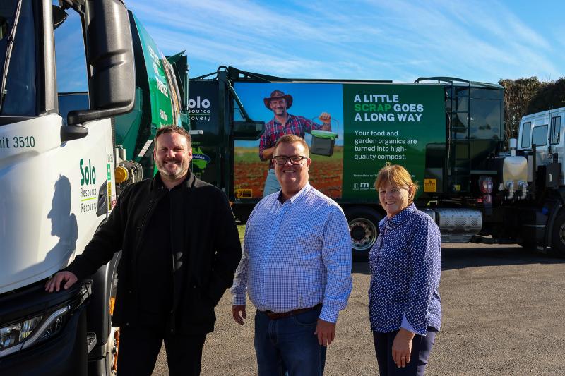 Three people stand in line smiling with large waste trucks in background with FOGO branding.