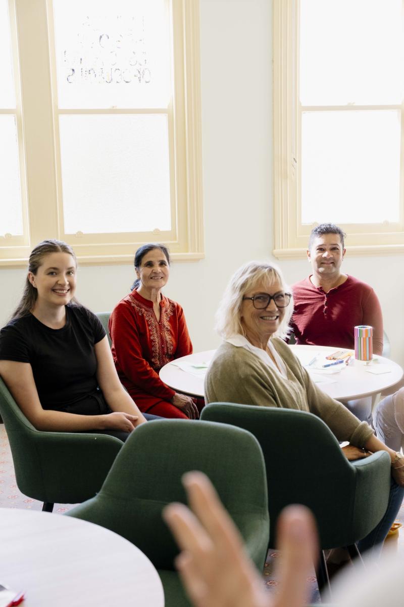 A group of four people sit around a table, looking at a person who is offscreen.