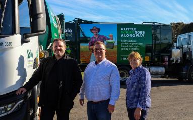 Three people stand in line smiling with large waste trucks in background with FOGO branding.