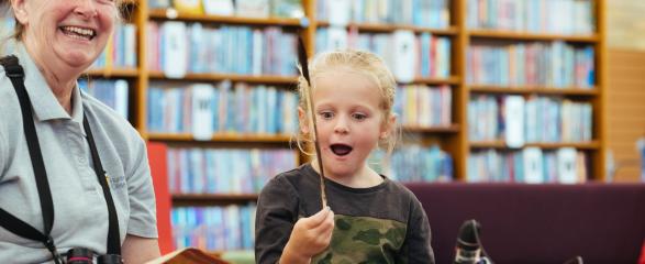 Child holding up a feather at a library