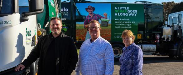 Three people stand in line smiling with large waste trucks in background with FOGO branding.