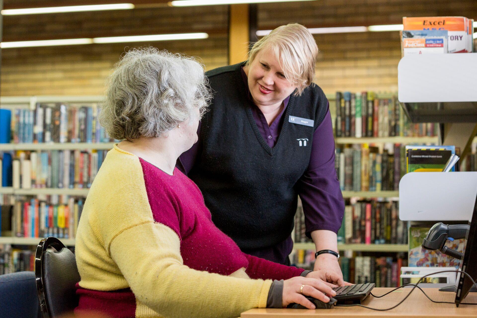 Library staff helping woman use a computer