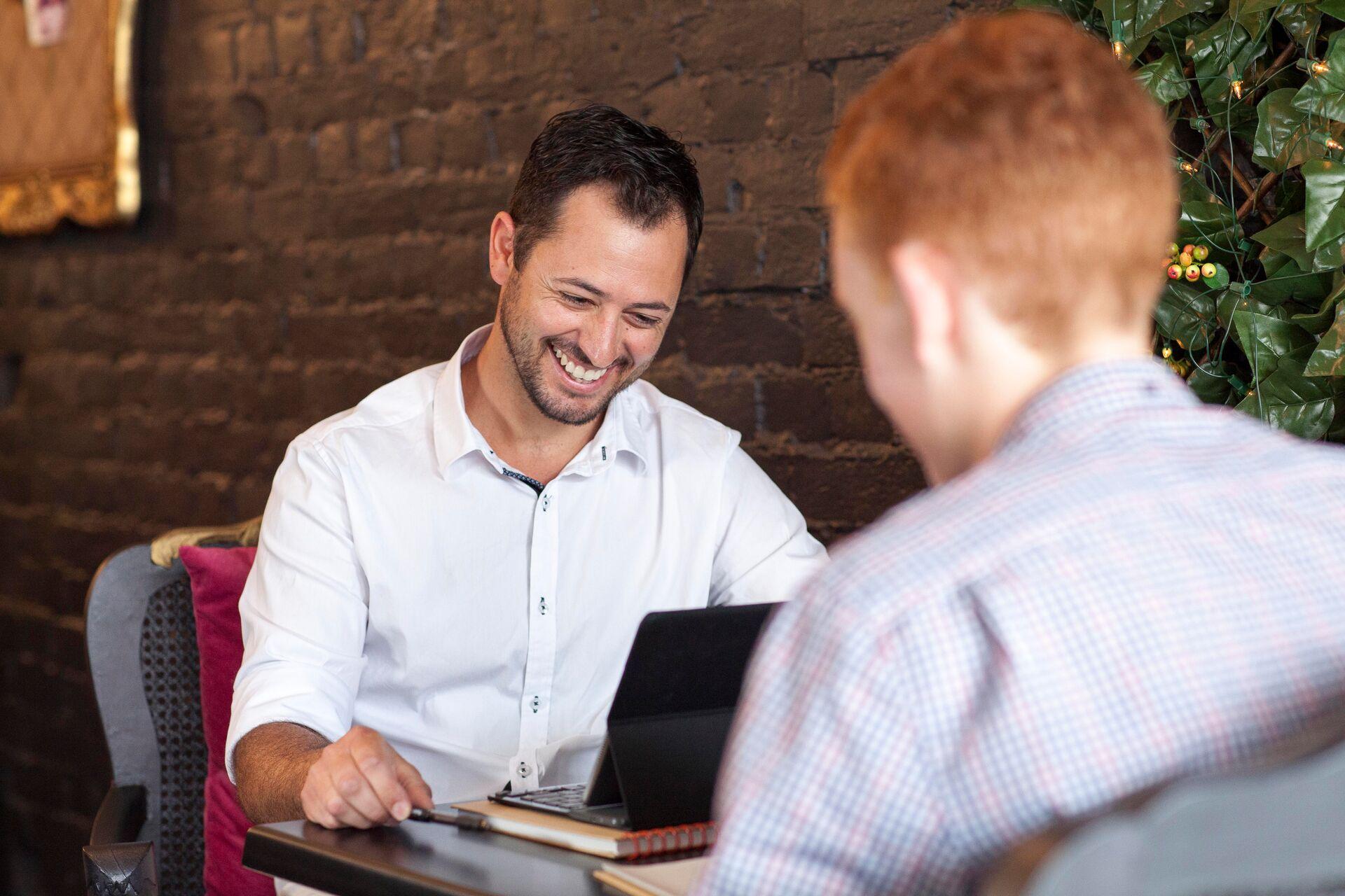 Two men smiling and working on laptop in cafe